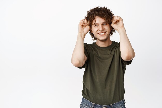 Joli jeune homme montrant un geste de pattes de chiot souriant et regardant heureux à la caméra debout en t-shirt sur fond blanc