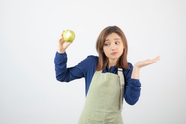 un joli modèle de jeune fille en tablier tenant une pomme verte fraîche.