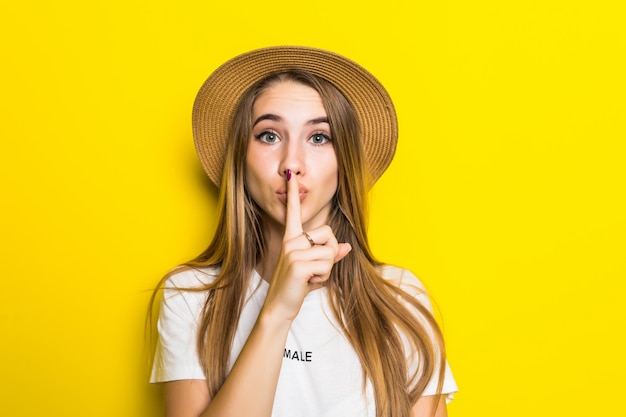 Joli modèle en t-shirt blanc et chapeau sur fond orange avec le doigt sur les lèvres