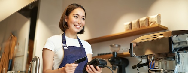 Photo gratuite une jolie barista asiatique dans un café qui traite des paiements sans contact insère une carte de crédit dans le terminal postal