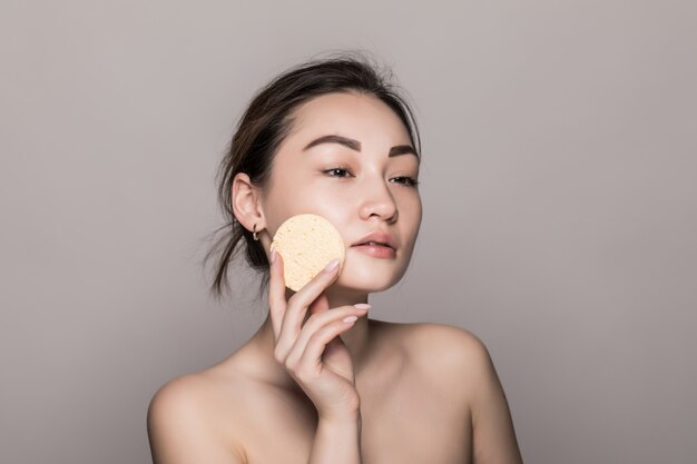 Jolie beauté jeune femme asiatique nettoyer son visage avec un coton sur blanc isolé sur mur blanc. Concept de peau saine et cosmétiques.