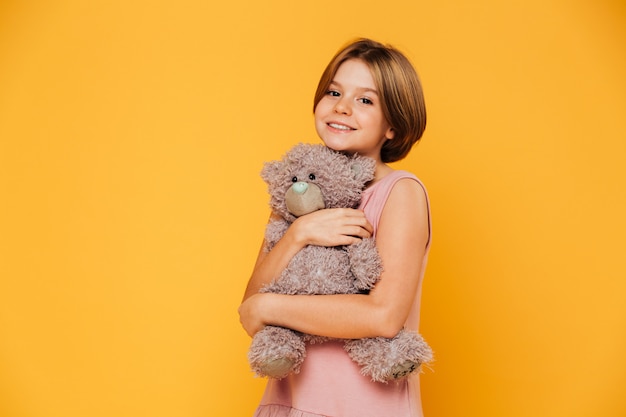 Jolie belle fille embrasse son ours en peluche et souriant à la caméra