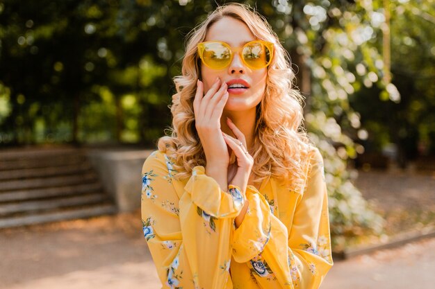 Jolie blonde élégante femme souriante en chemisier jaune portant des lunettes de soleil