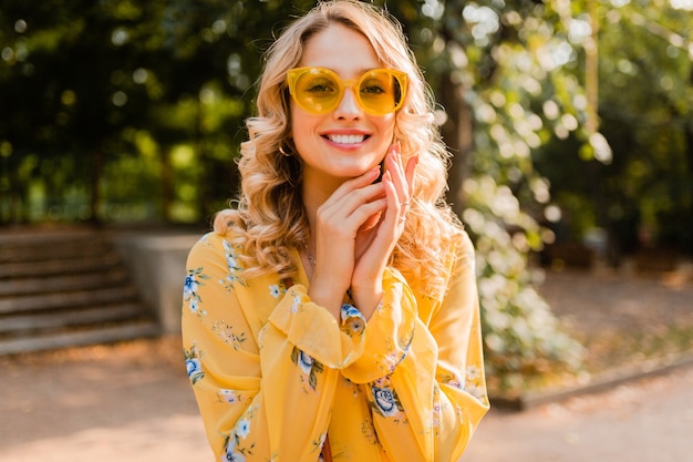 Jolie blonde élégante femme souriante en chemisier jaune portant des lunettes de soleil