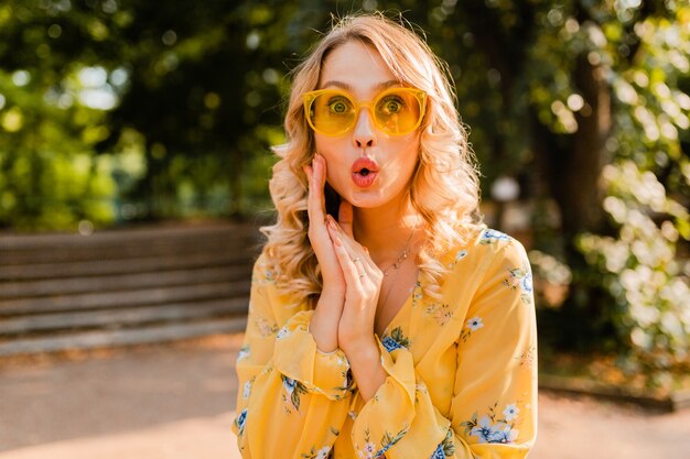 Jolie blonde élégante femme surprise en chemisier jaune portant des lunettes de soleil