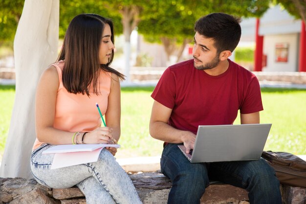 Jolie brune latine assise à côté d'un garçon à l'école et entamant une conversation