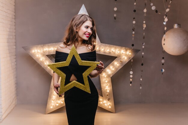 Jolie brune mince en attente de la fête du nouvel an. Fille en robe noire posant avec étoile brillante.