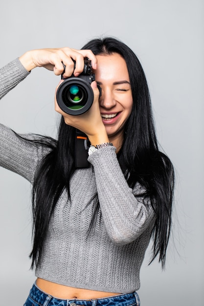 Jolie brune vise sa caméra. composer une photographie en studio, isolé sur mur gris