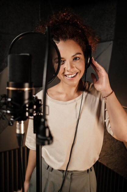 Jolie chanteuse dans les écouteurs regardant joyeusement à huis clos travaillant sur un nouvel album de musique dans un studio d'enregistrement sonore