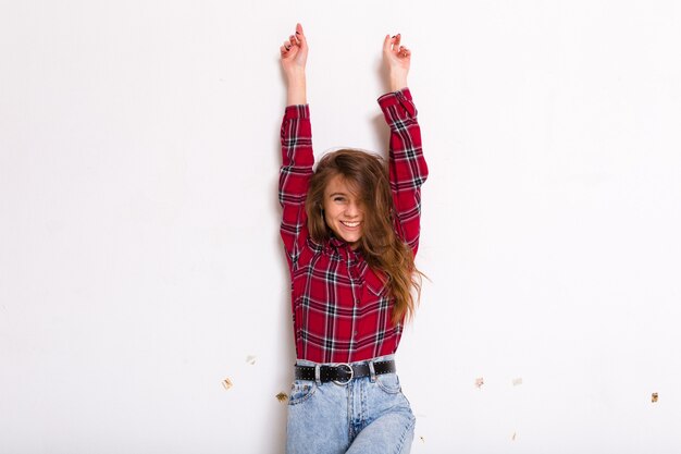 Jolie charmante jeune femme aux cheveux longs posant avec les mains et sourire portant une chemise rouge sur blanc