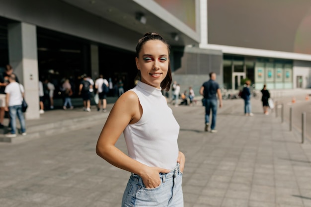 Jolie dame adorable avec un maquillage lumineux et un t-shirt blanc regarde la caméra Charmante se promène dans la ville par une chaude journée d'été