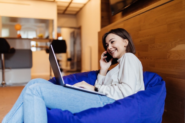 Jolie dame à l'aide de téléphone portable sur une chaise de sac au bureau créatif