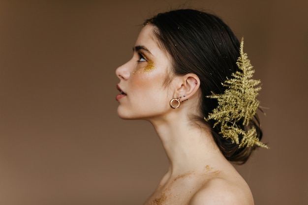 Photo gratuite jolie dame aux cheveux noirs avec une peau pâle regardant vers le haut. photo intérieure d'une fille debonair avec une feuille verte dans les cheveux.