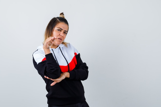 Jolie Dame Montrant Un Geste D'arrêt Avec La Paume Vers L'extérieur Dans Un Sweat à Capuche Et L'air Confiant. Vue De Face.