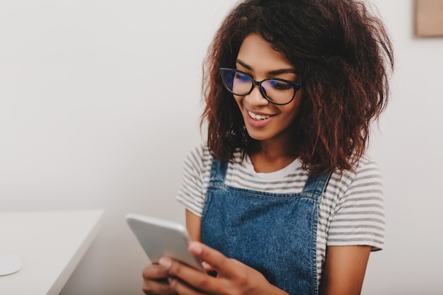 Jolie dame à la peau de bronze vérifiant les nouveaux messages sur les réseaux sociaux à l'aide de son téléphone