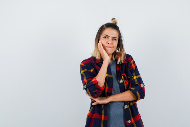 Jolie dame penchée sur la joue en chemise à carreaux et à la pensive