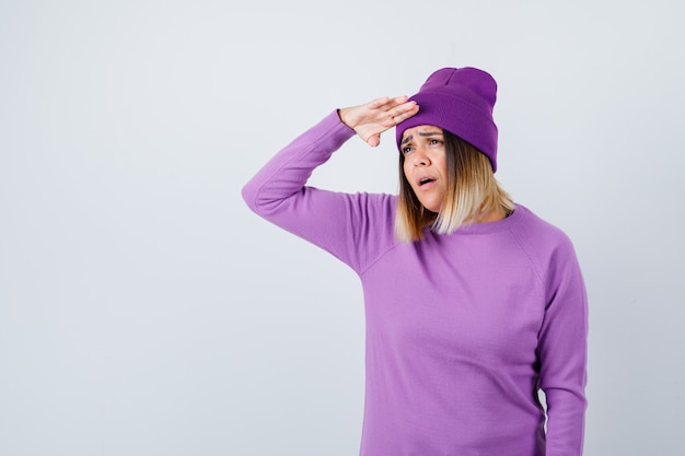 Jolie dame regardant loin avec la main sur la tête en pull, bonnet et l'air perplexe. vue de face.