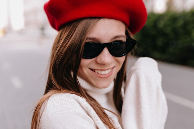 Jolie dame souriante en béret rouge et lunettes noires passe un bon moment en week-end d'automne