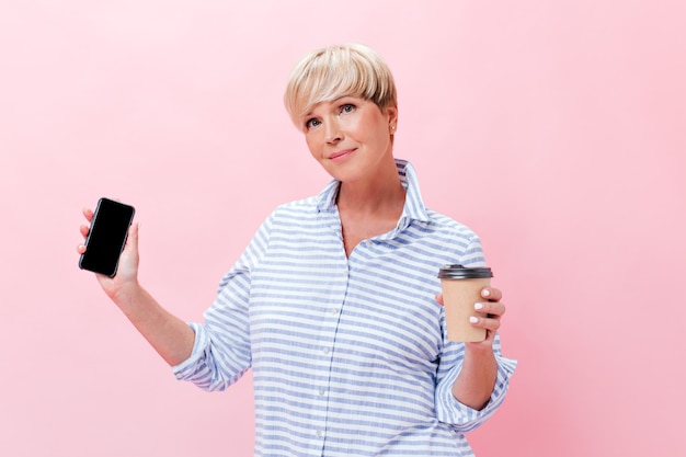 Jolie dame en tenue à carreaux tient une tasse de thé et un smartphone