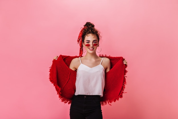 Jolie dame en veste rouge et lunettes de soleil se penche sur la caméra sur fond rose