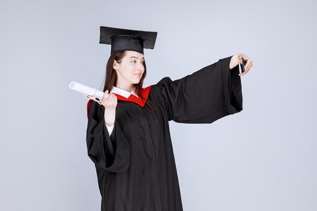 Jolie étudiante diplômée en robe prenant selfie. photo de haute qualité