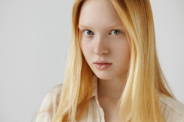 Jolie étudiante tachetée avec des traits délicats portant ses longs cheveux blonds lâches, se détendre à la maison après des cours à l'université, à la recherche d'un sourire subtil, les lèvres sont légèrement écartées