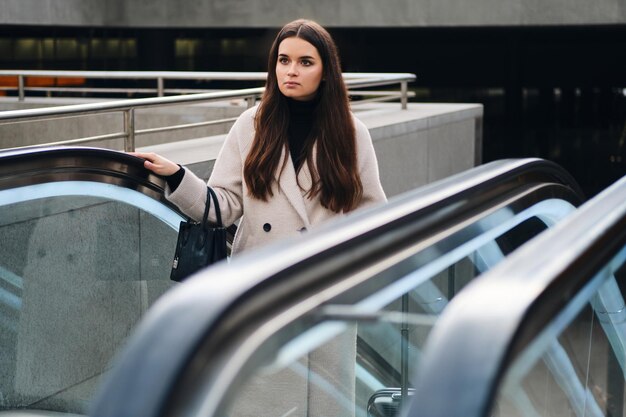 Jolie femme d'affaires élégante regardant pensivement sur l'escalator extérieur