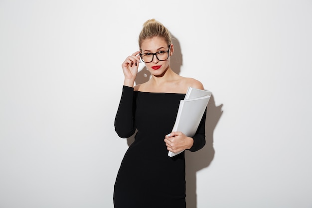 Jolie femme d'affaires en robe et lunettes tenant des documents