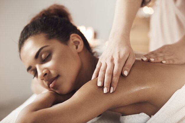 Jolie femme africaine ayant massage relaxant dans le salon spa. Yeux fermés.
