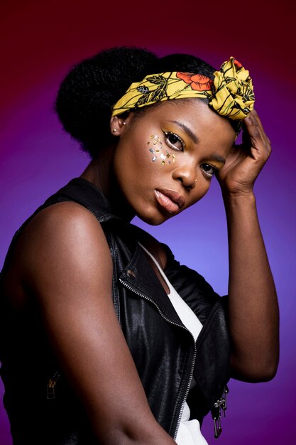 Jolie femme africaine en gilet en cuir avec des confettis brillants sur ses joues