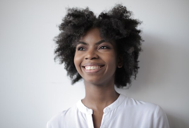 Jolie femme afro-américaine avec un large sourire debout sur un mur blanc