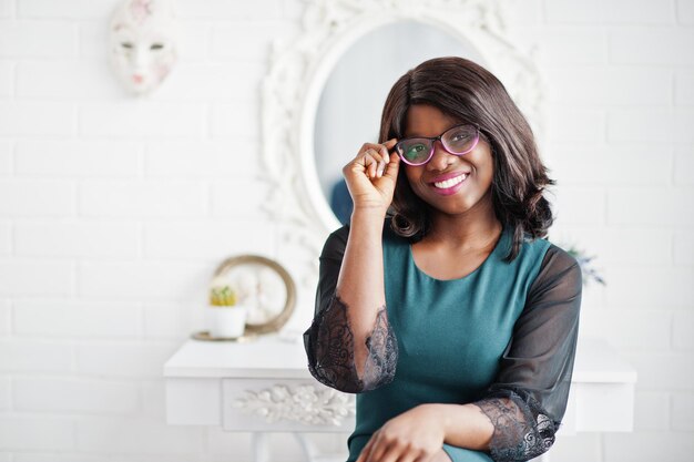 Jolie femme afro-américaine à lunettes posée dans la chambre contre le miroir