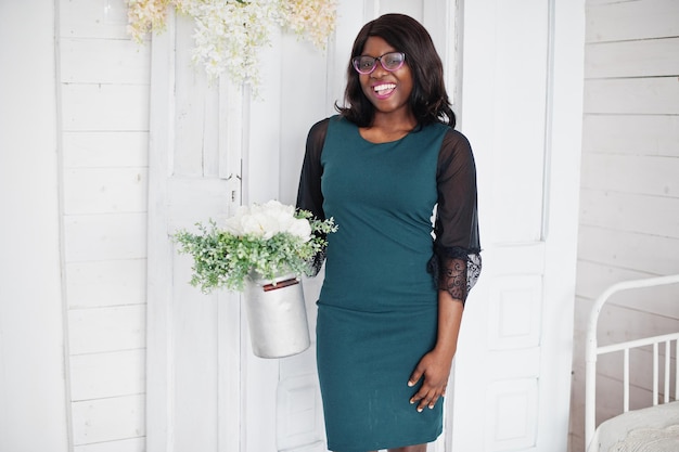 Jolie femme afro-américaine à lunettes posée dans la chambre avec pot de fleurs à la main