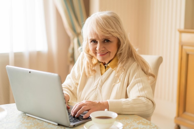 Jolie Femme âgée Devant Un Ordinateur Prend Une Tasse De Thé Et Profite Du Temps Libre