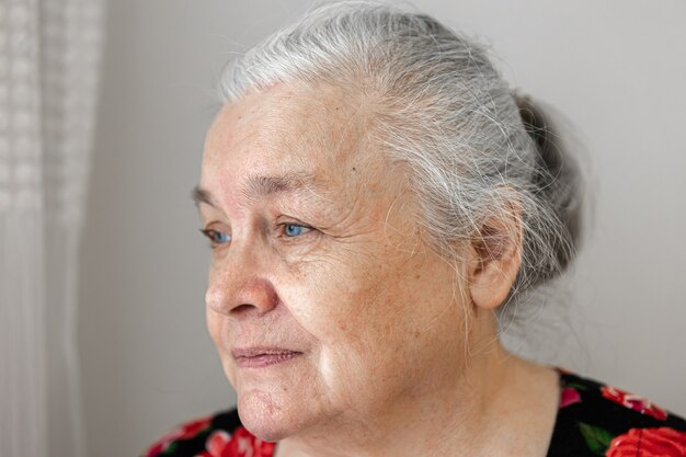 Jolie femme âgée avec tristesse regarde par la fenêtre se bouchent.