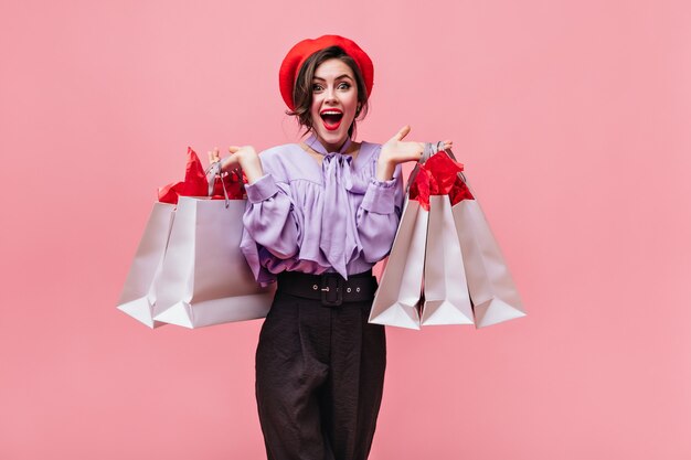 Jolie femme aime faire du shopping et pose avec des sacs. Portrait de jeune fille aux yeux verts avec des lèvres croustillantes sur fond rose.