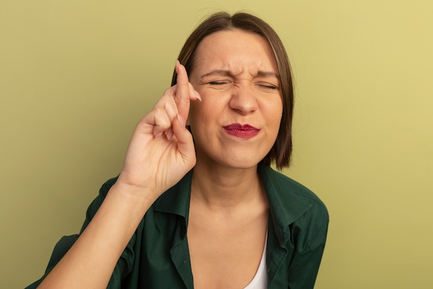 Photo gratuite jolie femme anxieuse se tient avec les doigts croisés isolé sur mur vert olive