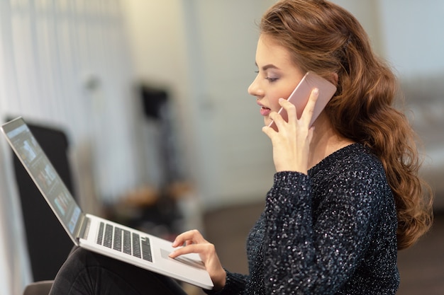 Photo gratuite jolie femme appelant par téléphone intelligent travaillant sur ordinateur. jeune femme avec téléphone portable et ordinateur portable.