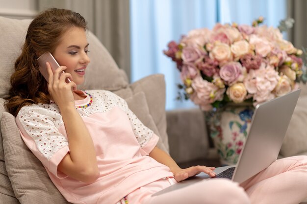 Jolie femme appelant par téléphone intelligent travaillant sur ordinateur. Jeune femme avec téléphone portable et ordinateur portable.