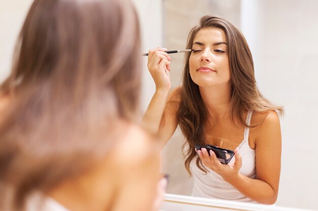 Jolie femme appliquant le fard à paupières devant un miroir