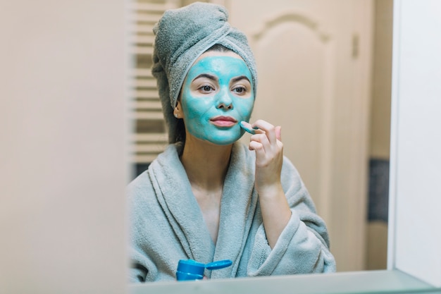 Jolie femme appliquant un masque près d&#39;un miroir