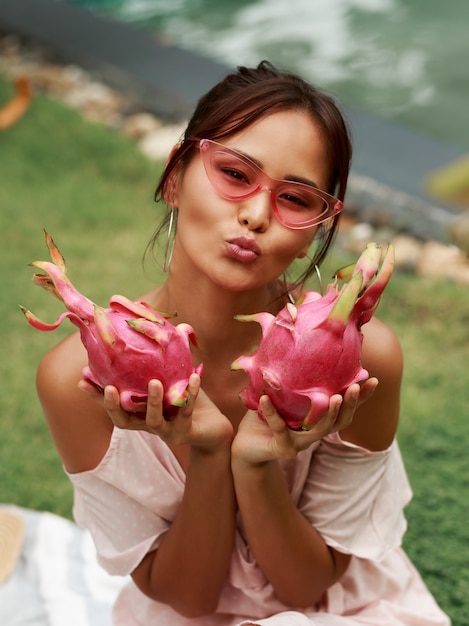 Jolie femme asiatique tenant des fruits du dragon rose dans les mains