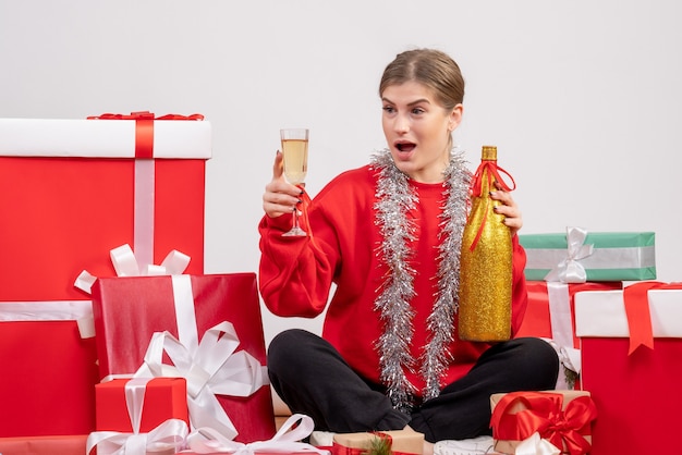 Jolie femme assise autour des cadeaux de Noël célébrant avec du champagne sur blanc