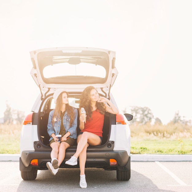 Jolie femme assise sur le coffre de la voiture