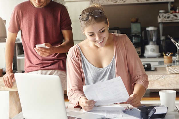 Jolie femme au foyer caucasienne tenant un morceau de papier, lisant une lettre de banque