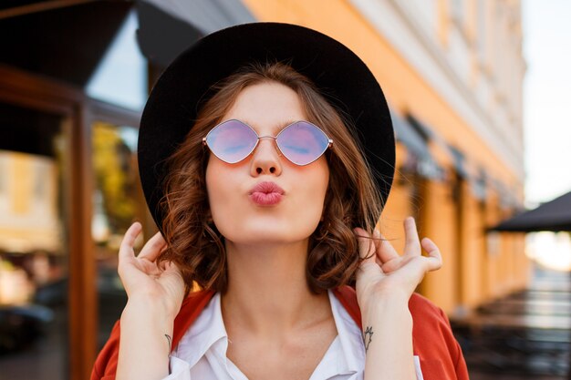 Jolie femme aux cheveux courts envoyant un baiser aérien. Look automne élégant.