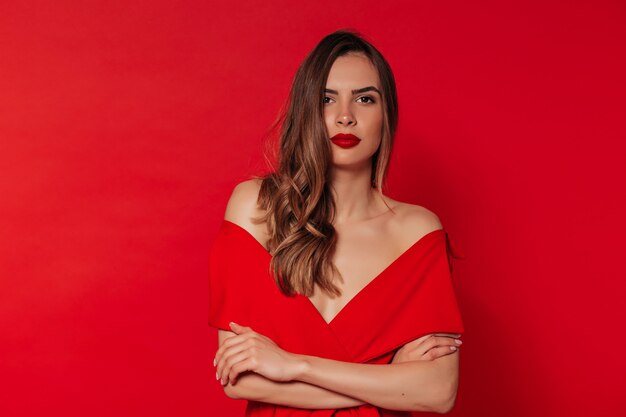 Jolie femme aux cheveux ondulés avec rouge à lèvres lumineux rouge en élégante robe d'été rouge souriant et posant sur isolé