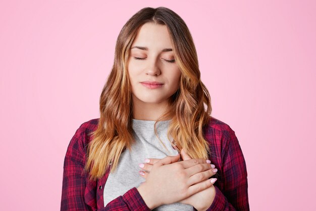 Jolie femme aux yeux fermés, garde les mains sur la poitrine, exprime sa sympathie à quelqu'un, reconnaissant à un ami proche