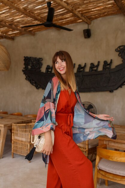 Jolie femme blanche en autfit bohème d'été élégant posant dans un café tropical.