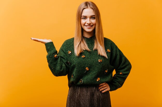 Jolie femme blanche avec une coiffure droite riant sur l'orange. Modèle féminin européen Winderful en pull vert bénéficiant de portraitshoot.